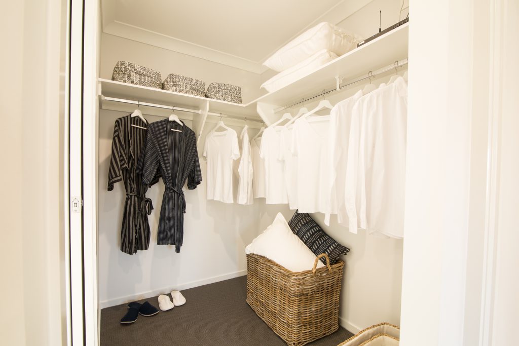 Walk-In-Wardrobe - Standard White Board Top Shelf & Chrome Hanging Rods with hanging robes and plain shirts.
