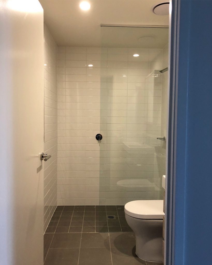 Frameless Panel in white tiled bathroom with brown tiled floor and toilet