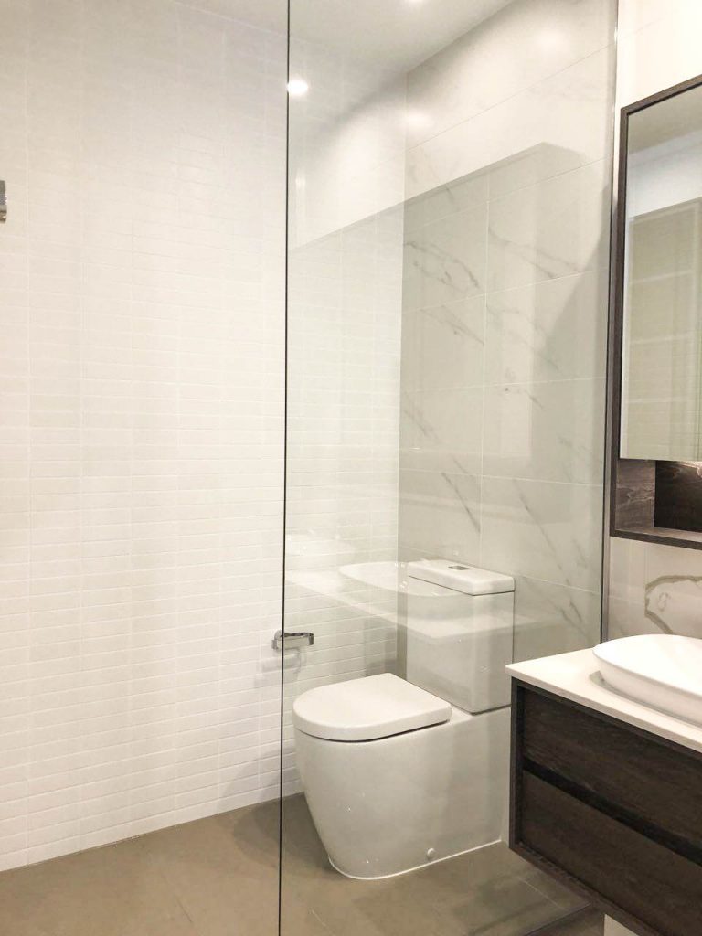 Frameless Panel in white bathroom beside matte brown cabinet and vanity