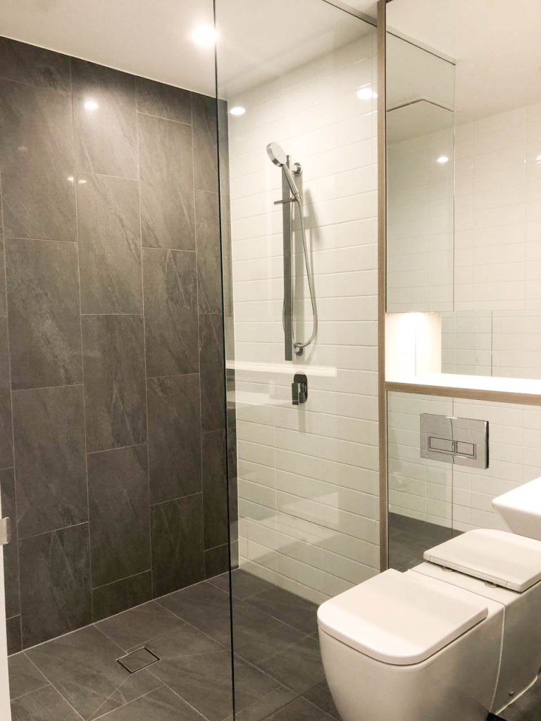 Frameless Panel in white tiled bathroom with brown tiled floor and toilet