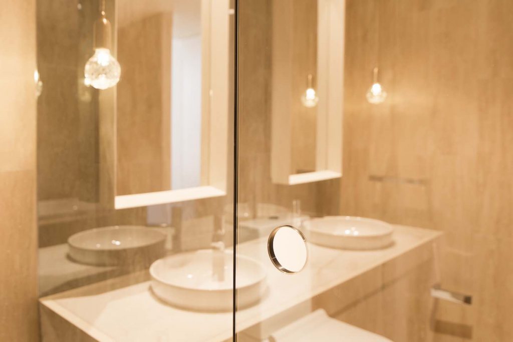 Frameless hinged shower Civic Abian T screen beside modern white vanity and warm bathroom lighting
