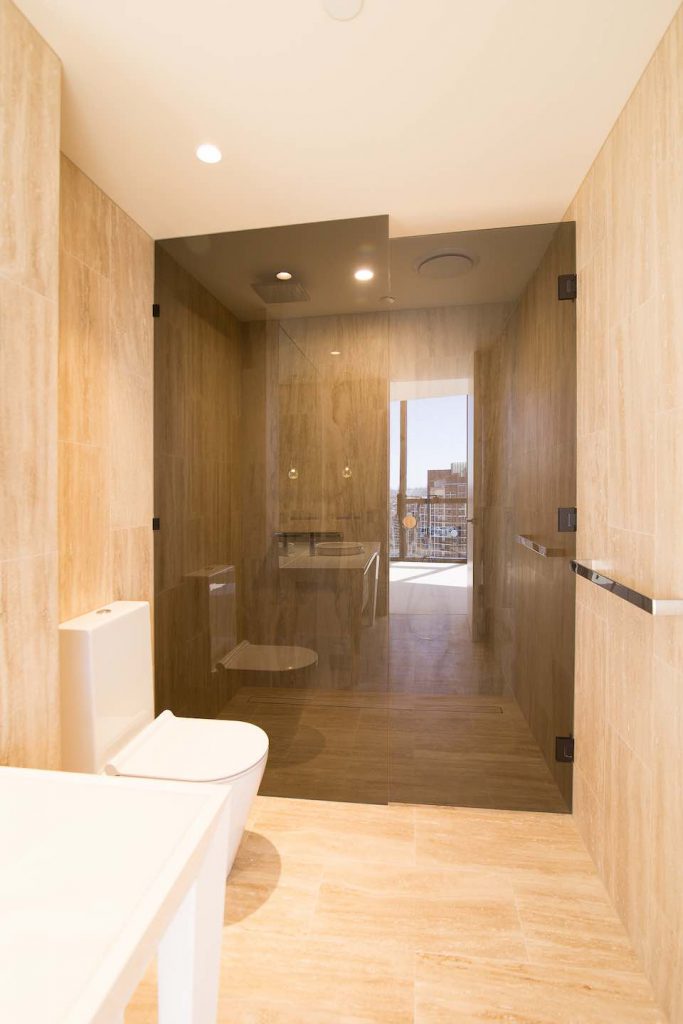 Frameless hinged shower Civic Abian T screen beside modern white vanity and warm bathroom lighting
