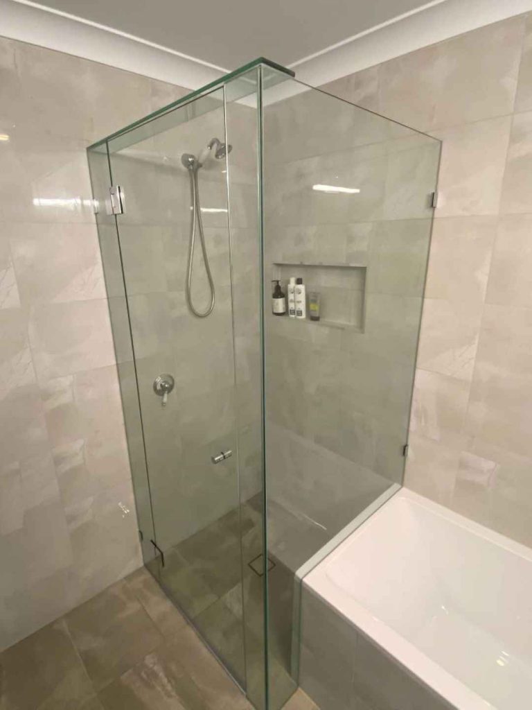 Frameless hinged shower beside bathtub with shower overhead